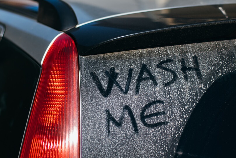 Dirty car window with “wash me” written on it highlighting importance of cleaning car windows